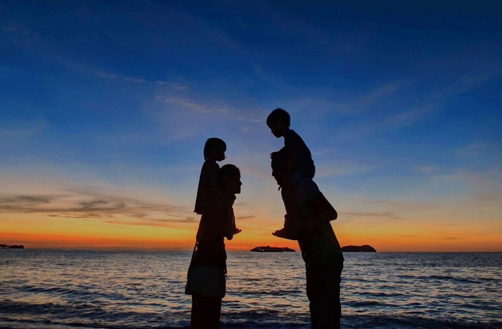 The Ultimate Parenting Checklist by Dr. Alison Escalante uses uncommon wisdom to make your parenting life easier. Family walking on the beach with parents holding young children on their shoulders.