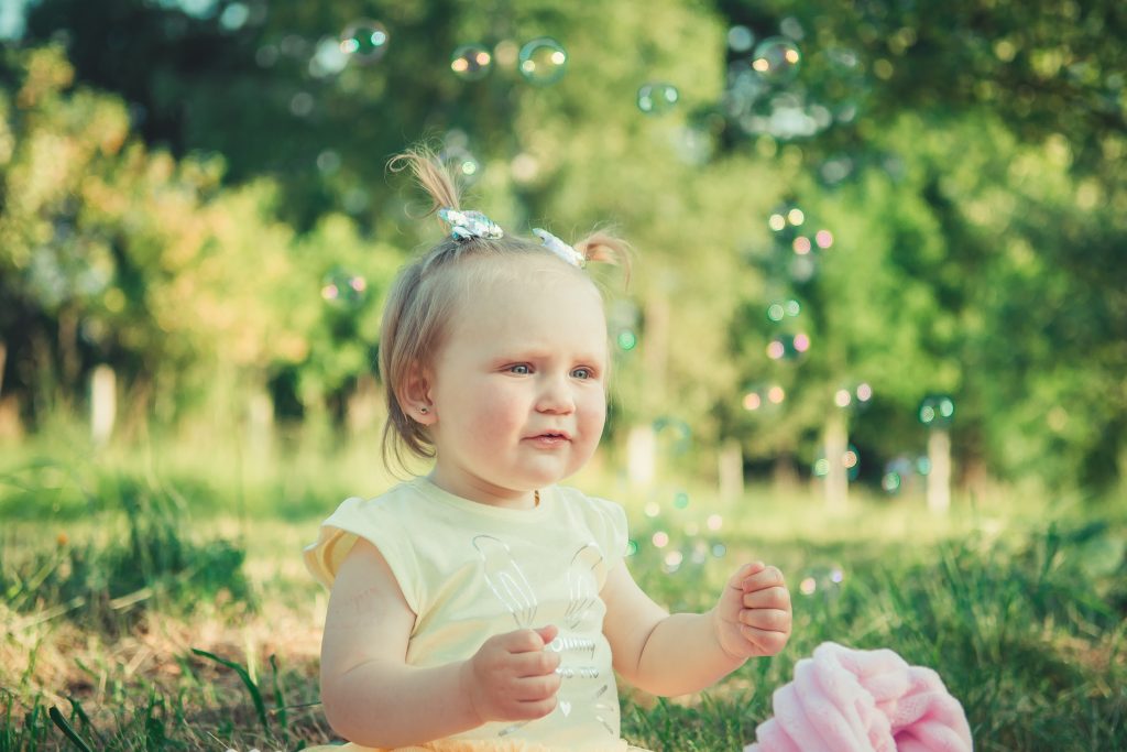 Toddler girl outdoors looking at bubbles.